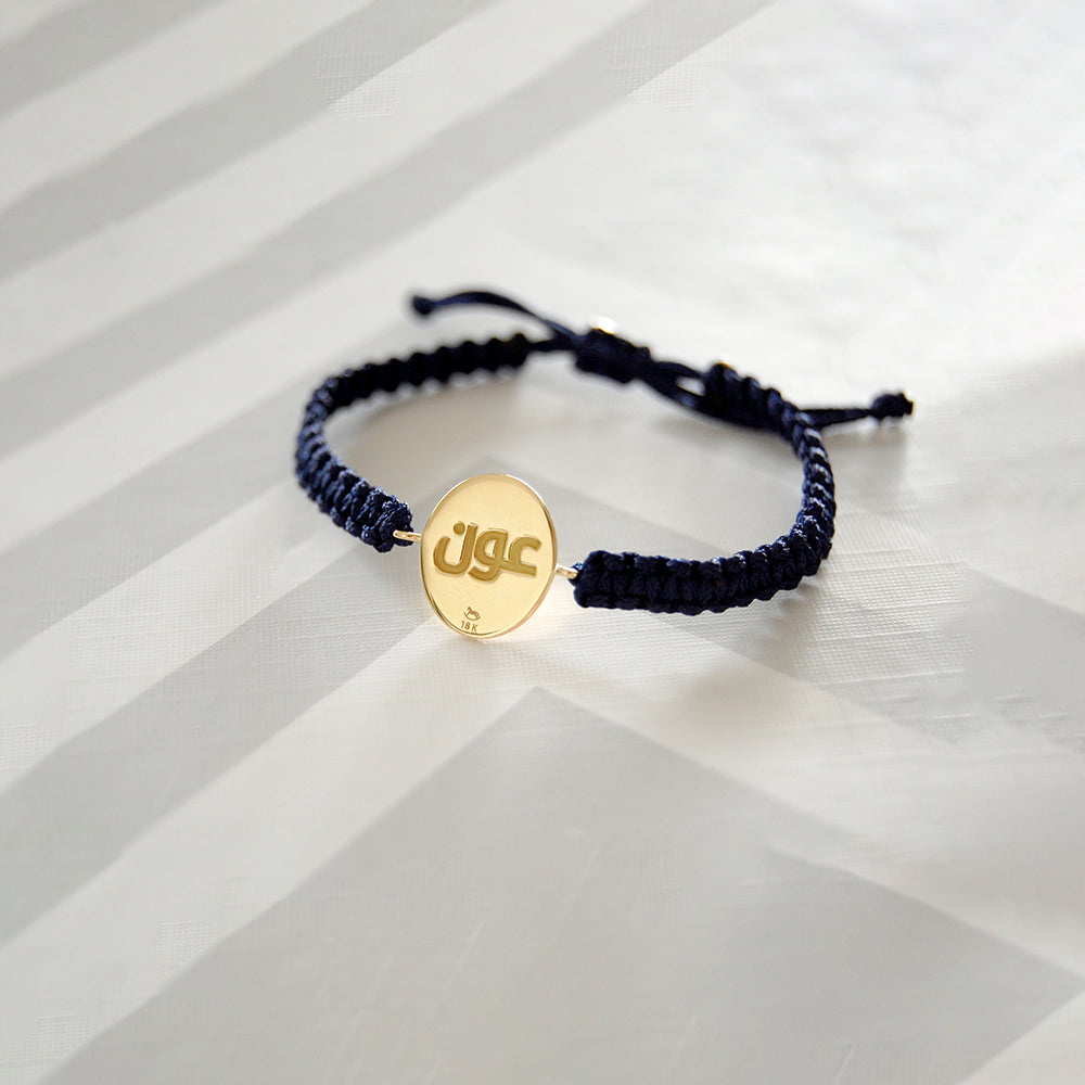 A Customised Navy cord bracelet with oval 18K gold disc engraved with Ayat Al-Kursi