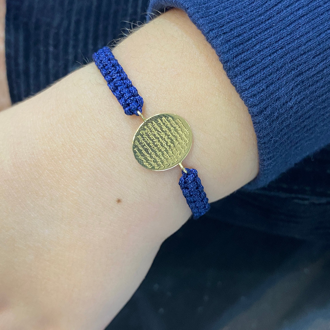 A warn navy cord bracelet with Oval 18K gold disc engraved with Ayat Al-Kursi