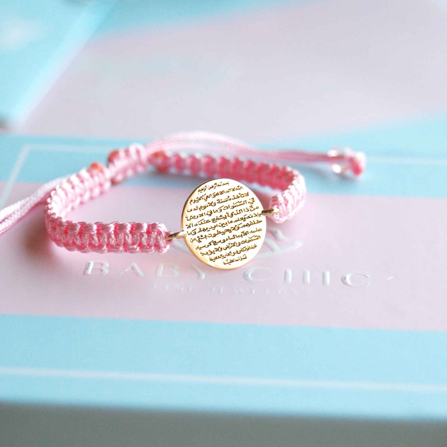 Pink Ayat Al Kursi bracelet with gold oval charm displayed on Baby Chic gift box