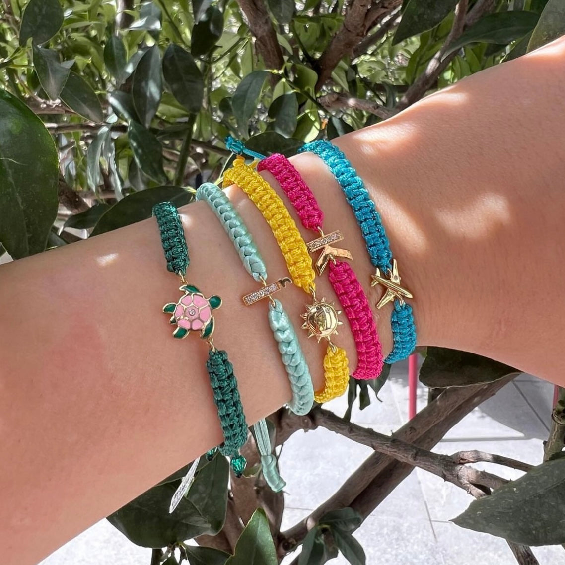Colorful braided cord bracelets with gold charms worn on wrist outdoors