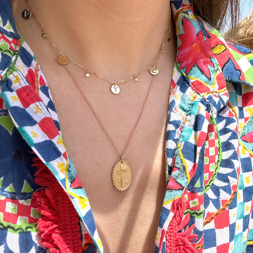 Gold layered necklaces with letter charms and floral oval pendant on colorful blouse