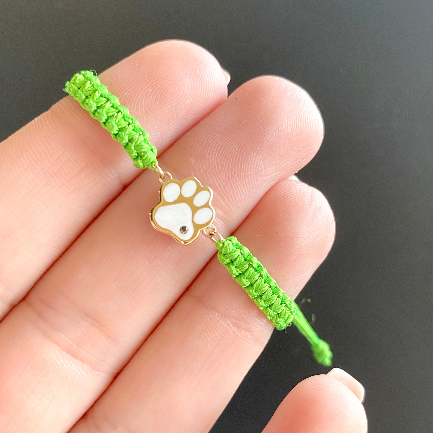 Green cord Brave Paw bracelet with gold and white enamel paw charm shown on hand