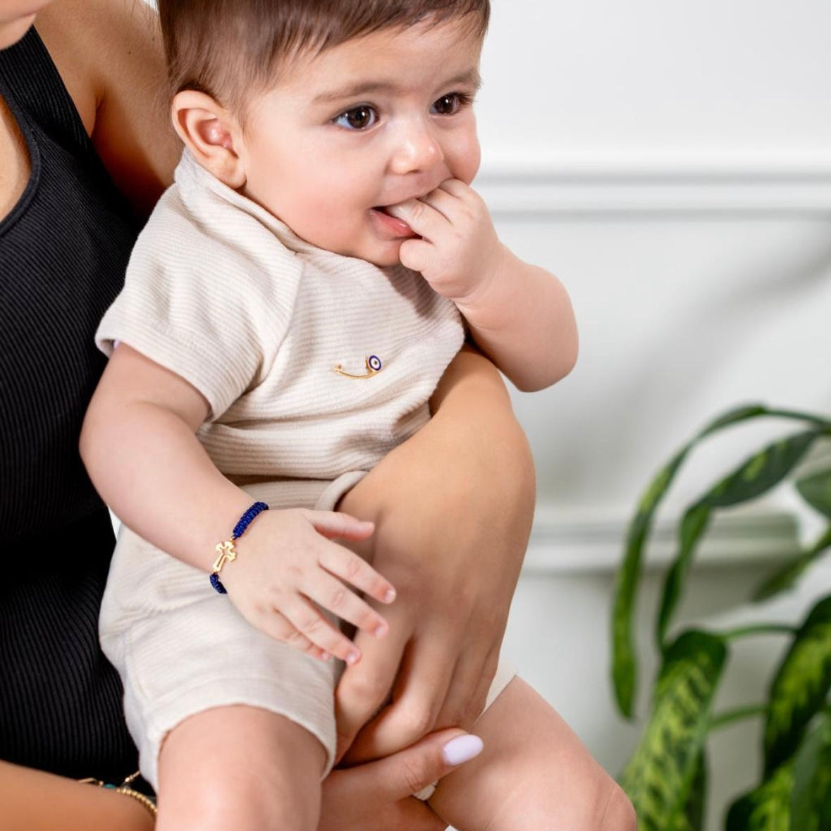 Baby wearing navy cord bracelet with gold cross charm