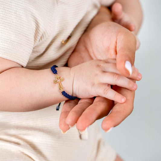 Gold cross cord bracelet worn on baby wrist