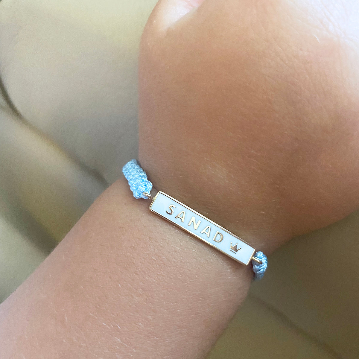 Personalized name plate bracelet worn on wrist with blue cord