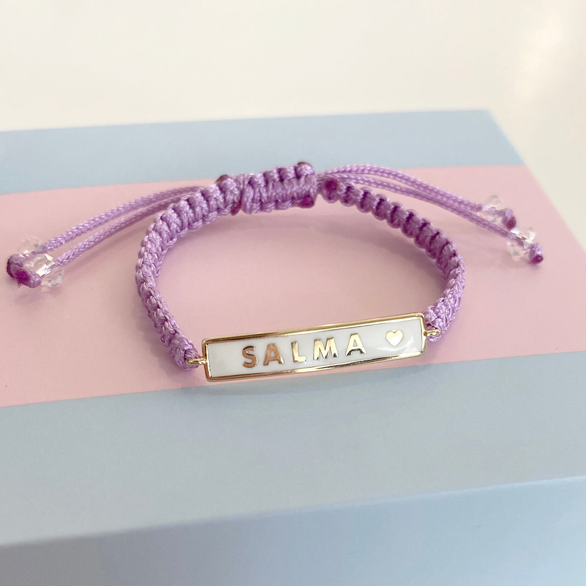 Custom name plate bracelet with purple cord displayed on surface