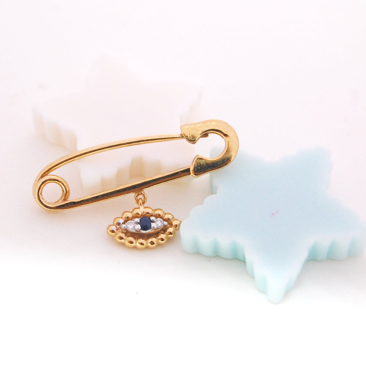 Yellow gold baby safety pin with evil eye charm and blue center stone