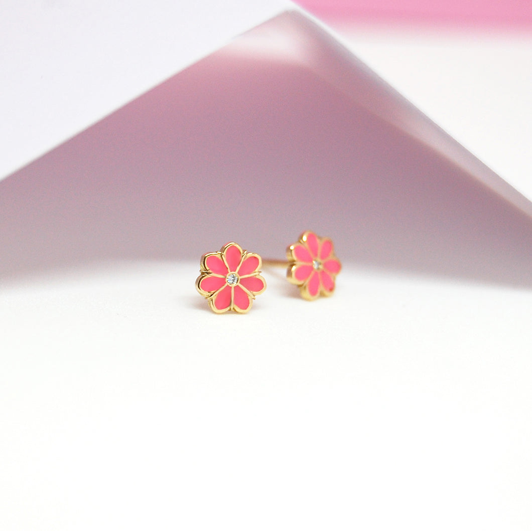Gold Lily Earrings with pink enamel petals and diamond centers placed under soft pink lighting for a dreamy, delicate display.