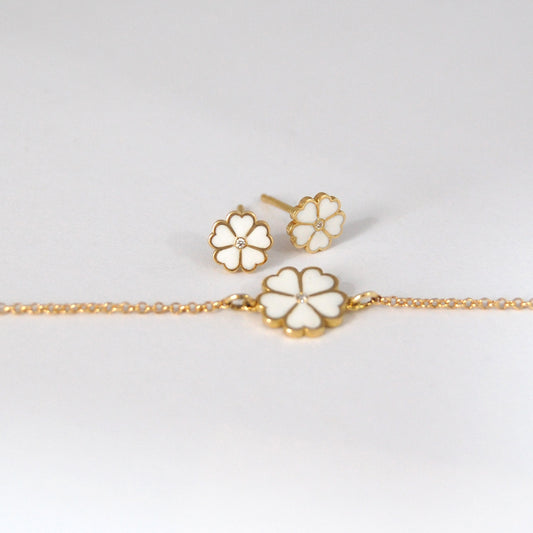 Lucky Clover bracelet and matching stud earrings in white enamel and gold, arranged elegantly on a white surface.