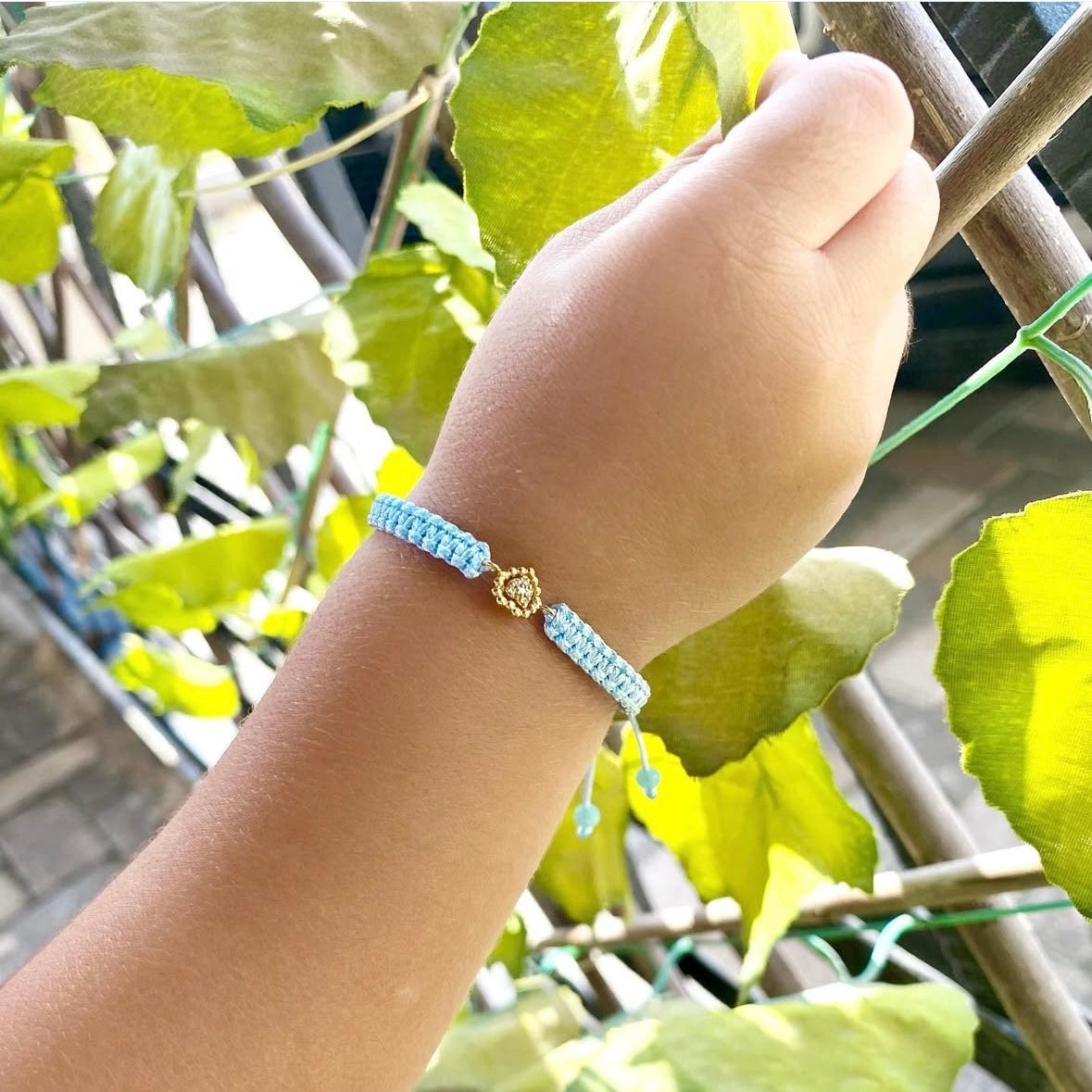 Light blue Sweetest of Hearts diamond bracelet worn on a child’s wrist, set against a leafy outdoor background.