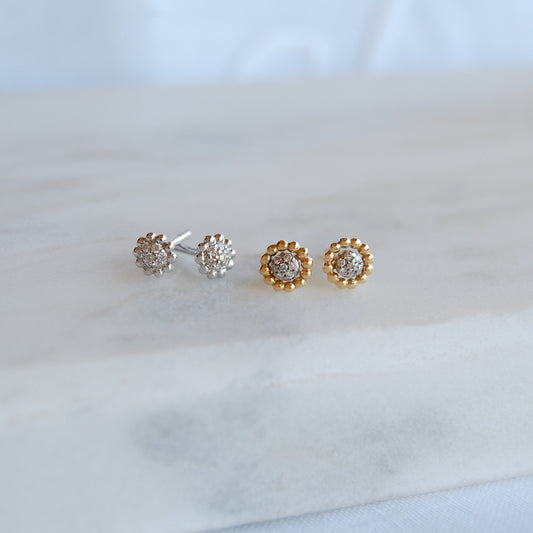 Two pairs of All Around Diamond Earrings—one in yellow gold, one in white gold—displayed on a soft marble surface.