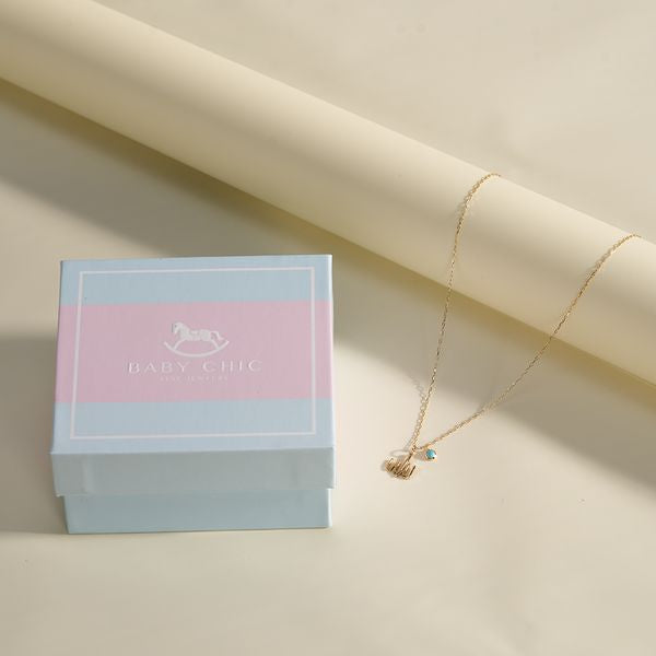Gold necklace with “Allah” Arabic calligraphy pendant and turquoise charm displayed next to a BabyChic gift box on a cream background.
