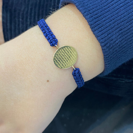 A warn navy cord bracelet with Oval 18K gold disc engraved with Ayat Al-Kursi 