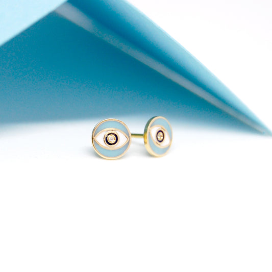 Blue Nazar Diamond Earrings resting against a folded blue background, showcasing the enamel eye design accented with diamonds in the center.
