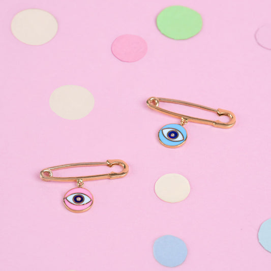 Two brooches with eye designs on a pink background with colorful polka dots