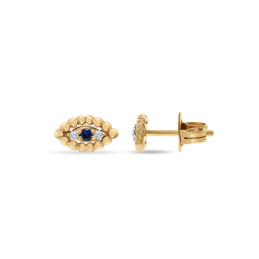 Pair of gold stud earrings shaped like an evil eye, with a central blue sapphire and two flanking white diamonds, surrounded by gold bead detailing, displayed on a white background.