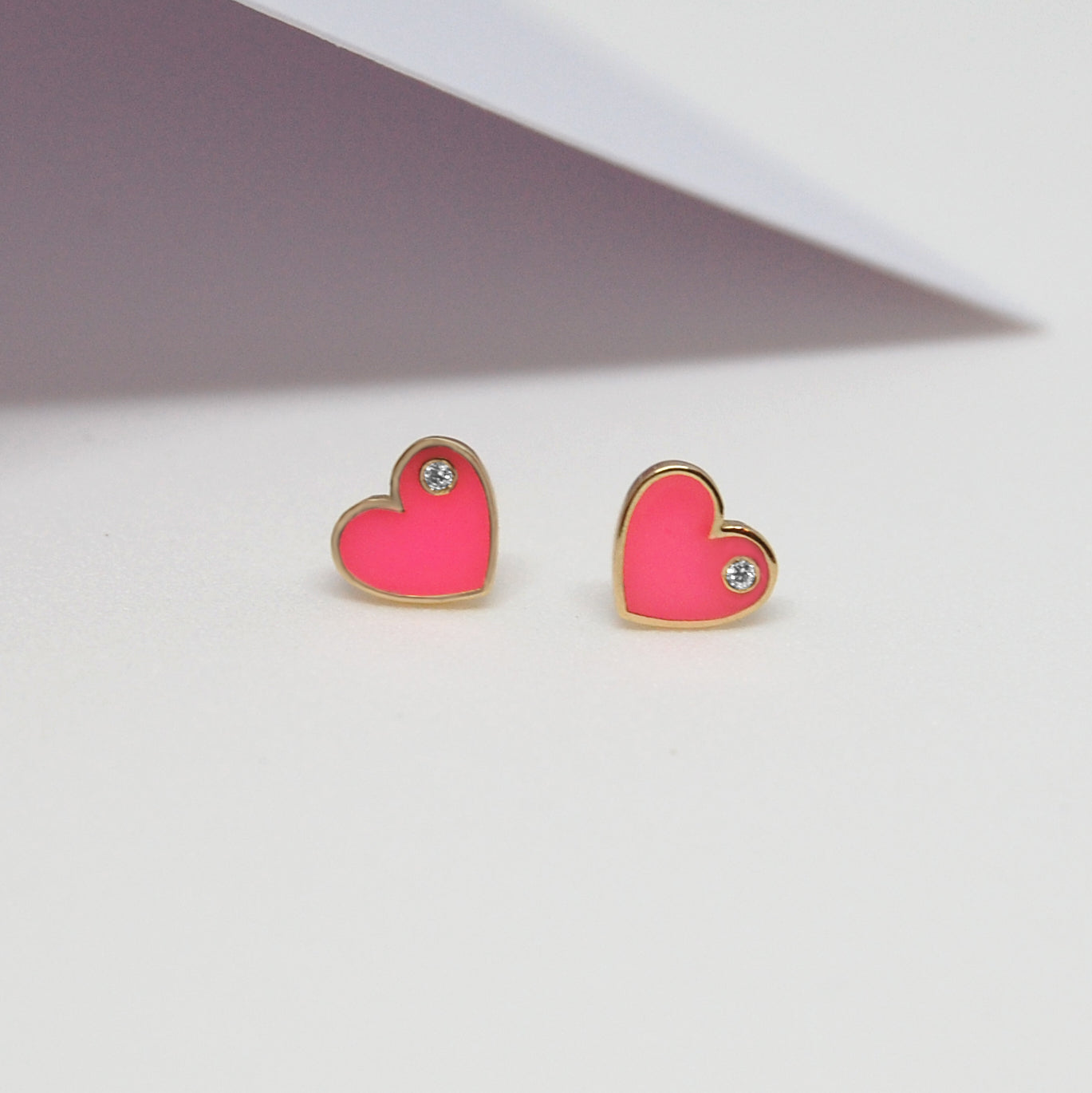 Close-up of Forever Love Earrings in pink enamel with gold trim and sparkling diamonds, styled on a white surface.