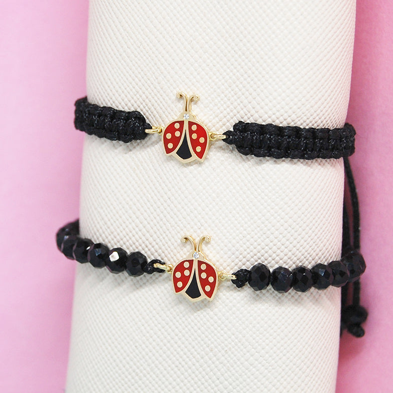 Close-up of a black cord bracelet showcasing a gold and red ladybug charm with a diamond accent.