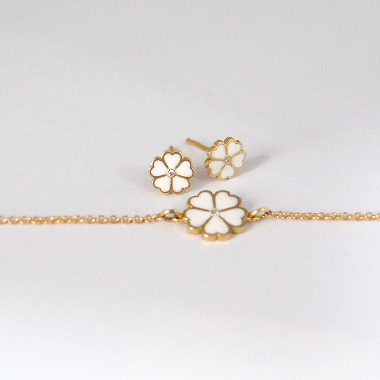 Lucky Clover bracelet and matching stud earrings in white enamel and gold, arranged elegantly on a white surface.