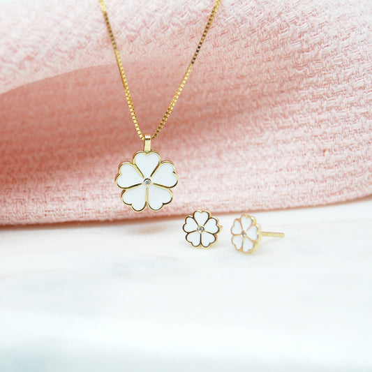 Lucky Clover jewelry set featuring a gold necklace with white enamel flower pendant and matching stud earrings, styled against soft pink textured fabric.
