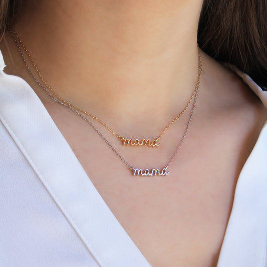 Two delicate “mama” script necklaces worn layered on the neck—one in yellow gold and one in white gold—displayed against skin and a white blouse.