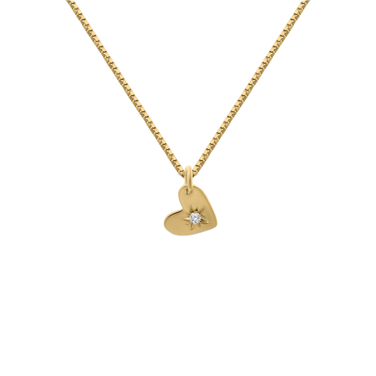 A studio shot of a delicate 18K yellow-gold heart pendant featuring a starburst engraving set with a single round brilliant-cut diamond, suspended from a fine paper-clip chain on a transparent background.