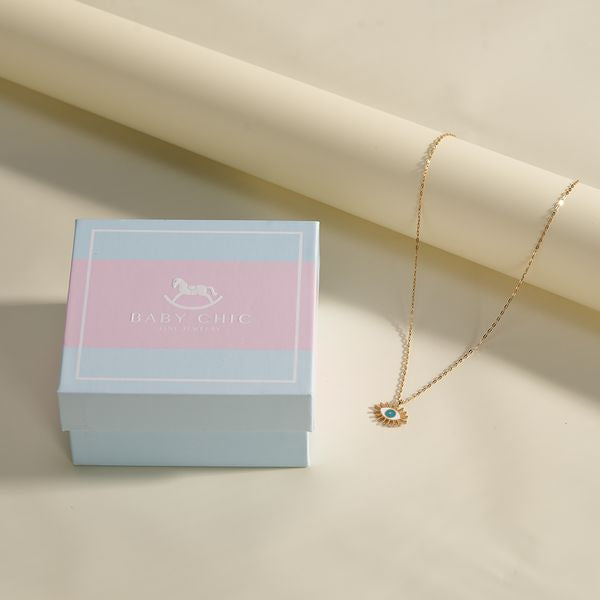 18K gold eye necklace with turquoise enamel and diamond center, next to Baby Chic Jewelry gift box.