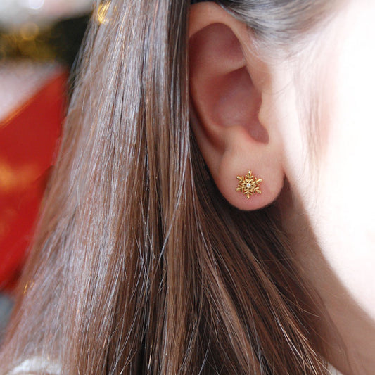 Close-up of a gold snowflake-shaped earring with a central diamond worn on an earlobe.