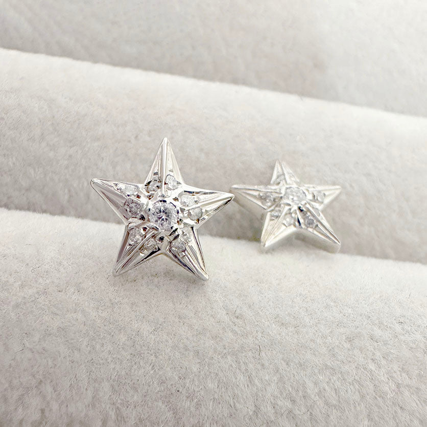 Close-up of white gold star-shaped earrings with diamond accents, displayed on a soft beige jewelry tray.