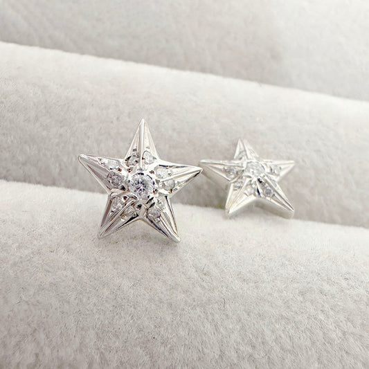 Close-up of white gold star-shaped earrings with diamond accents, displayed on a soft beige jewelry tray.