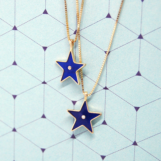 Two gold star-shaped enamel necklaces with centered diamonds, displayed on a blue geometric background.