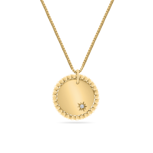 A studio shot of an 18K yellow-gold scalloped-edge coin pendant on a fine paper-clip chain, featuring a small starburst engraving set with a single round brilliant-cut diamond, shown on a transparent background.