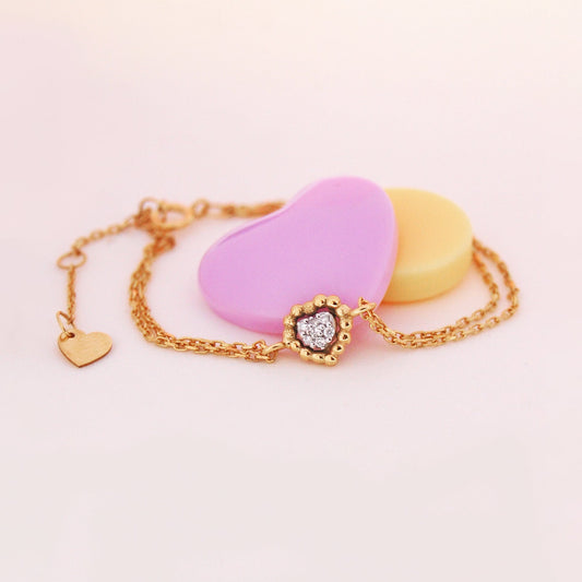 Sweetest of Hearts Diamond Bracelet in 18K gold, featuring a dainty heart-shaped cluster of diamonds on a double-chain design, styled with pastel heart props.