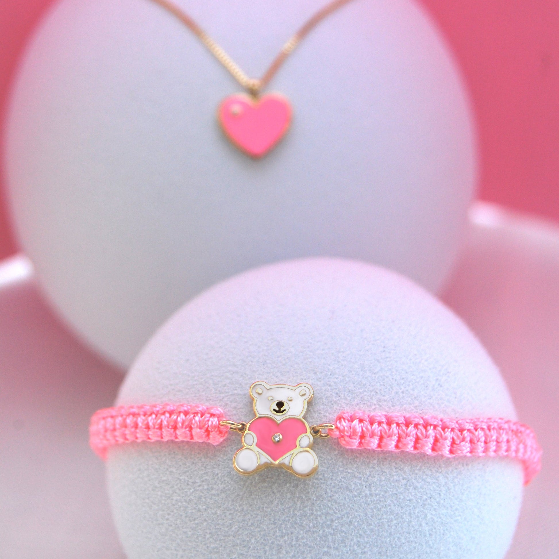 Necklace with a pink heart charm and bracelet with a bear charm on white balls against a pink background