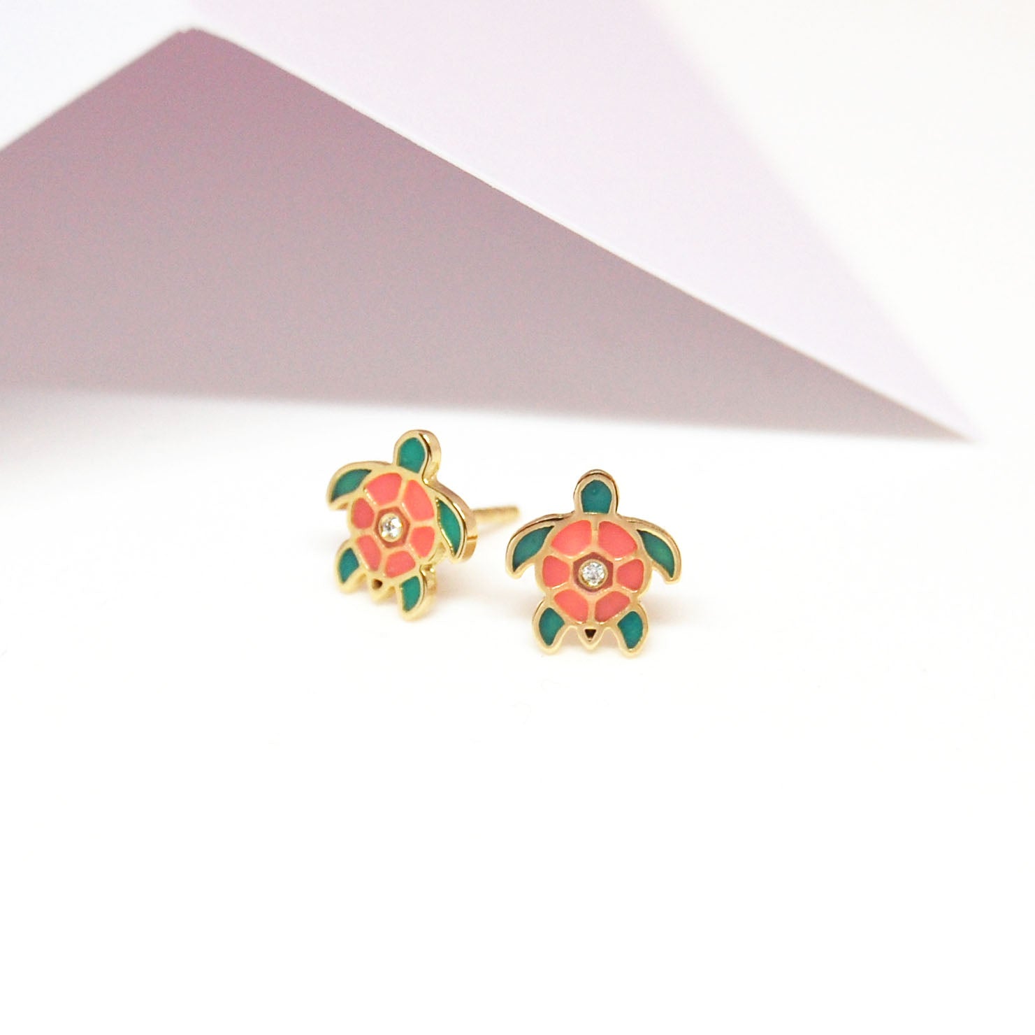 A pair of turtle-shaped earrings with pink and green enamel and a small diamond in the center.